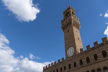 Fototapeta premium Palazzo Vecchio clock tower in Florence under blue sky. View of the iconic Palazzo Vecchio clock tower in Florence, Italy. Historic architecture and medieval landmark in the city center with a bright 