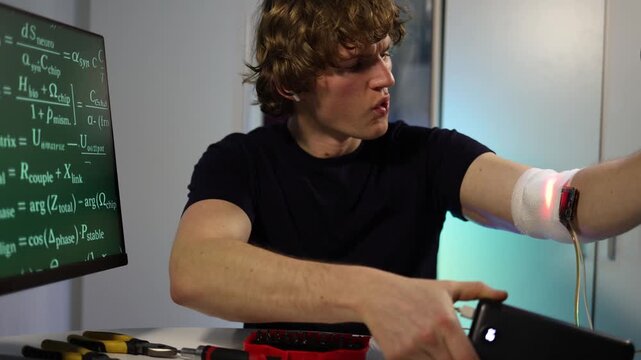 Young engineer adjusts glowing arm implant while coding neural systems in futuristic home lab with digital equations tools and intense creative focus and precision