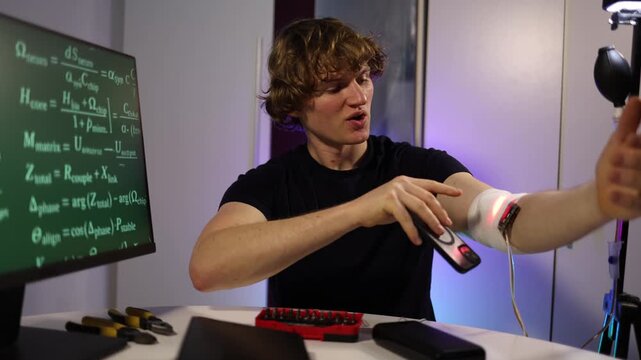 Young biohacker records himself while testing glowing wearable sensor on his arm tracking live data in a futuristic lab with intense experimental mood
