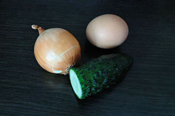Fresh ingredients: onion, egg and cucumber on a dark surface.