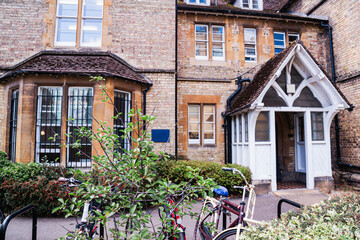 Exterior view of a traditional university college building in Oxford, featuring historic brick architecture, a small gabled entrance and bicycles parked nearby, reflecting daily academic life 