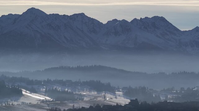 Aerial drone view of the Tatra Mountains from Czarna Gora near Zakopane, showing winter mountain range, forested hills, village landscape and alpine scenery during calm evening light
