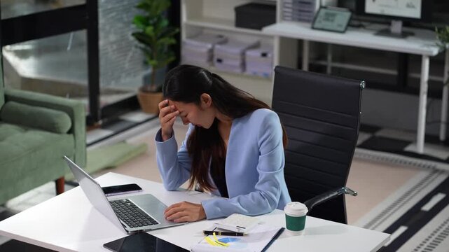 Young sad businesswoman is sitting at table, covering his face with his hand and talking on cell phone. On desk is laptop, tablet computer, Stress.