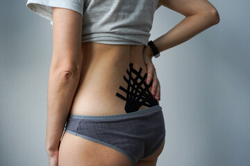     Rear view of a person with black kinesiology tape applied in a fan-shaped pattern to their lower back for muscle support and therapy.