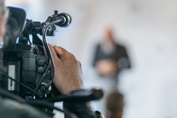 TV camera recording official statement at press conference. Captures structured communication, clarity, and professional media documentation.