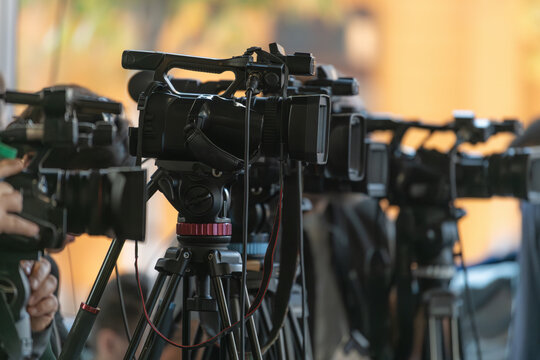 Multiple TV cameras positioned in a row capturing press event. Emphasizes organized media presence and professional audiovisual recording.