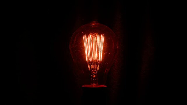 Close-up of a vintage incandescent light bulb glowing with a warm red light in darkness