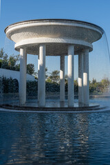 Futuristic, curved structure of fountain "Rotunda" with cascading water curtains and columns, reflecting in pool below. Rotunda fountain is in Cloud Park. Krasnodar Public Park or Galitsky Park