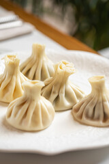 Traditional steamed khinkali dumplings with pleated dough served on a white plate in a bright interior