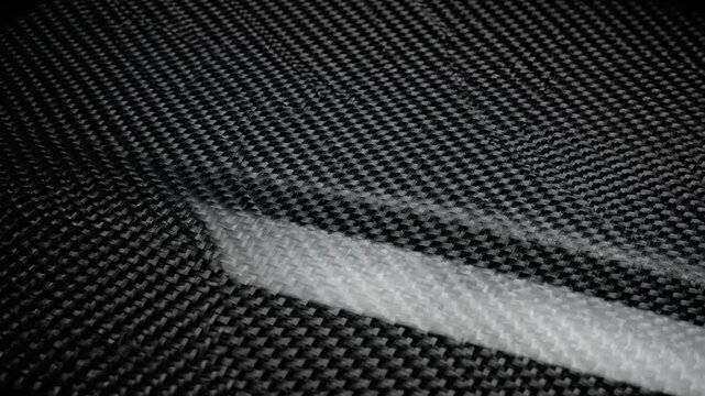Close-up of dark carbon fiber material, showcasing intricate woven texture and reflective surface. This advanced composite symbolizes strength, innovation, and modern engineering