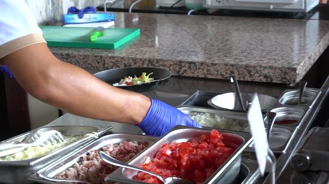 A chef prepares food in a restaurant. He adds chopped tomatoes, chopped onions, bell peppers, and mushrooms to a hot frying pan. Slow motion video. Perfect for cooking and food preparation content.