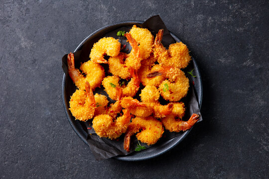 Crispy prawns on dark plate, tempting seafood appetizer for menu showcase. Grey background. Close up. Top view.
