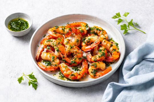 Grilled shrimps with chimichurri sauce on a white plate. Light grey background. Close up.