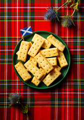 Scottish shortbread cookies on a plate with thistle flower and Scotland flag. Tartan textile background. Top view.