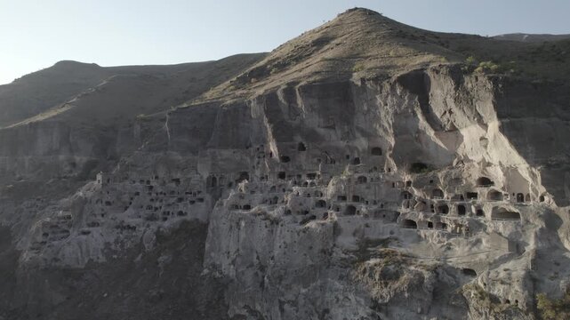 Aerial view of Vardzia, the ancient cave monastery town carved into rock in Georgia, captured at sunset with the sun visible on the horizon