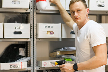 Male worker scanning package on storage shelf. Employee in white shirt using scanner while retrieving item from rack in fulfillment area