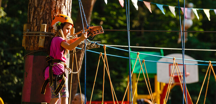 Happy school girl enjoying activity in a climbing adventure park on a summer day