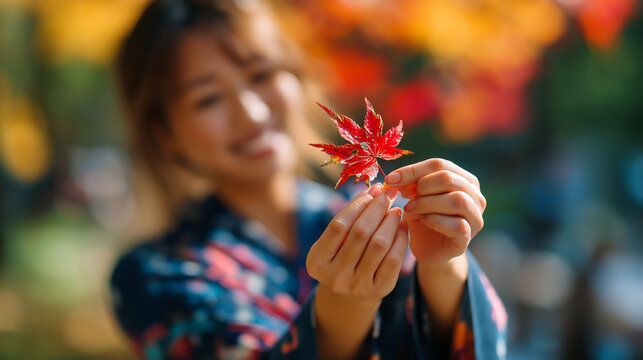 Faceless woman in autumn kimono holding red maple momiji leaf, fall season appreciation, defocused colorful foliage background, with copy space