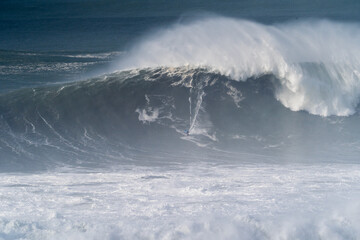 Dramatic scene of a surfer riding a massive big wave in Nazar&eacute;, Portugal, photographed at Praia do Norte, known for world-class big wave surfing.
