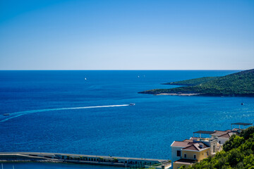 Obraz premium A scenic view of the Adriatic Sea in Montenegro. Clear blue waters stretch to the horizon, with a green hillside and coastal houses visible.