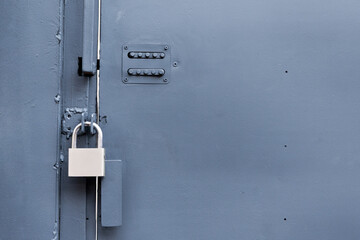 Gray metal door offering security and controlled access, featuring a closed padlock and an old mechanical keypad