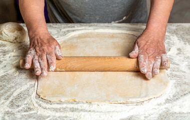 Female hands roll out a dough with a rolling pin. Closeup of man rolling dough with rolling pin for homemade bakery at table. Chef preparing a dough with a rolling pin