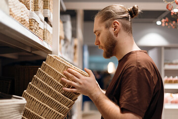 Young man selecting a woven basket or storage organizer in a home goods store.