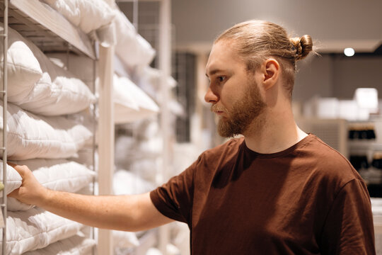Young man selecting a pillow in a home goods store, testing comfort, softness.