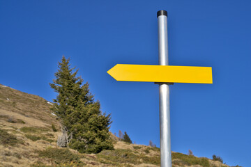 Yellow arrow sign pointing left providing copy space. Blank yellow arrow signpost on a metal pole showing direction against a clear blue sky.