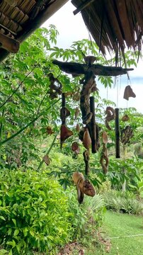 Ambient motion of a wind chime made of shells and twigs swinging gently in the breeze while hanging from a nipa hut, creating calm and soothing island life vibes