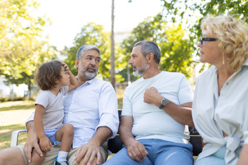 Grandparents and grandchild having conversation sitting on park bench