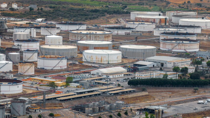 Fototapeta premium An industrial chemical plant or refinery from an aerial view, showing numerous large white and yellow storage tanks connected by intricate pipelines, set within a complex processing facility.