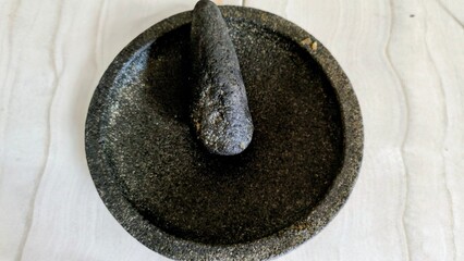 Top view of a traditional black stone mortar and pestle on a tiled surface.