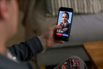 Young adult Caucasian man holding smartphone, browsing dating app with profile of young adult Caucasian woman smiling on screen, using technology for online dating interaction