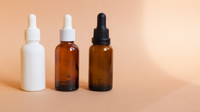 Different serum cosmetic bottles, white and dark brown dropper bottle container and packaging skincare product. studio pastel light background.