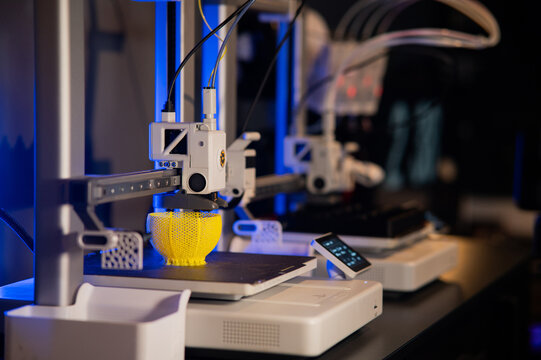Modern 3D printer printing a yellow lattice sphere object. Process of additive manufacturing and rapid prototyping in a high-tech workshop. - Powered by Adobe
