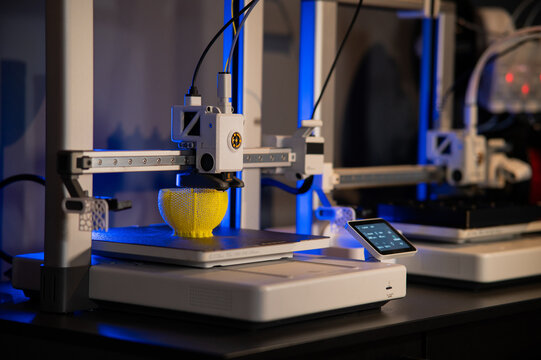 Close-up of 3D printer nozzle printing a yellow lattice sphere object. Additive manufacturing process in a high-tech laboratory.