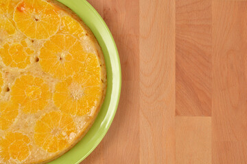 A delicious orange upside down cake on a green plate sits on a wooden table with copy space to the right