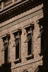 Vertical image of the exterior of a beautiful historical building made with stones and wooden window frames with shutters for the sun outdoor at daytime in the city centre of Adelaide in Australia.