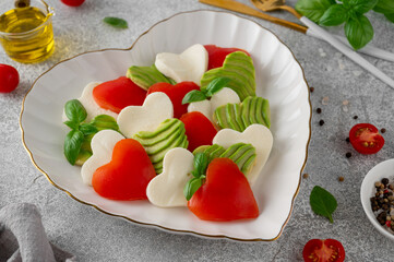Heart-shaped caprese salad with mozzarella, tomatoes, avocado and basil. A salad for Valentine's Day or Mother's Day. Top view, copy space.
