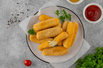 Crispy breaded mozzarella sticks on a plate with parsley, served with ketchup and mustard dips. Golden fried texture, appetizing snack on gray background
