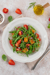 Healthy salad with strawberries, tomatoes, arugula, halloumi cheese and basil on a plate on a concrete background. Top view, copy space.