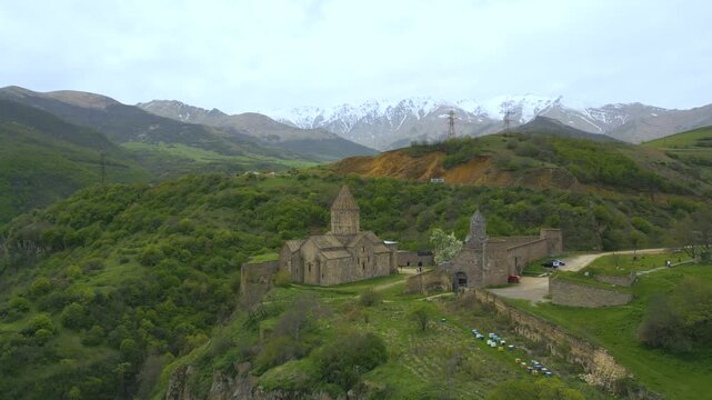 Aerial drone video of tatev monastery perched on dramatic cliff in armenia, revealing ancient stone architecture, green valleys and distant snowy mountains with smooth cinematic camera motion