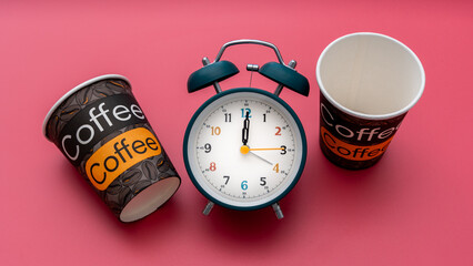 Teal retro alarm clock flanked by two takeaway coffee cups on vibrant red backdrop symbolizing...
