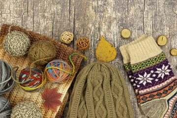 Knitting yarn, hat, scarf, and socks on a wooden background. There's space for text. Autumnal mood. Knitting is a form of handicraft.