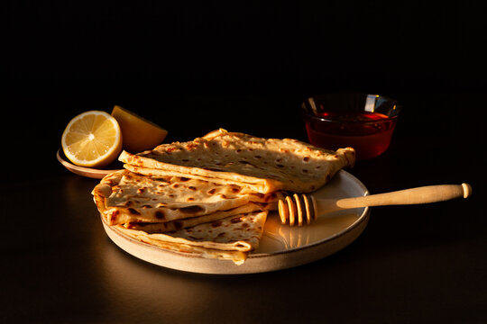 Assiette de cr&ecirc;pes sucr&eacute;es pli&eacute;es en triangle pour la chandeleur ou mardi gras, miel, un citron coup&eacute; en deux, ambiance chaleureuse et gourmande, vue de face en l&eacute;g&egrave;re plong&eacute;e, arri&egrave;re-plan brun fonc&eacute;