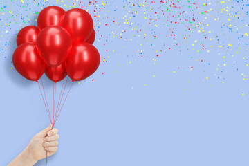 Female hand holding bunch of shiny red or pink balloons on blue background with confetti. Empty space for text