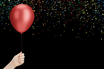 Female hand holds red balloon on black background with confetti. Empty space for text