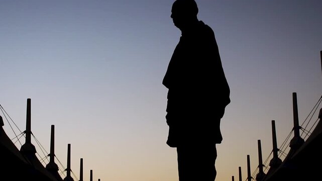 Statue of Unity in Gujarat at sunset, glowing orange and gold under dramatic sky. Scenic view highlights towering monument symbolizing national unity and cultural heritage.