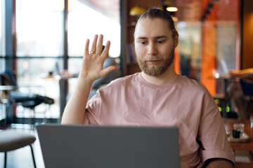 Obraz premium Young man waving at laptop screen during online meeting.